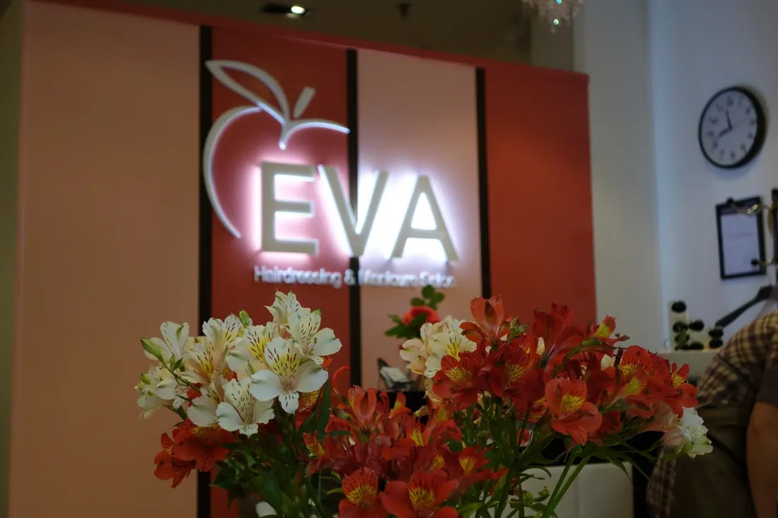 The illuminated EVA apple sign at the original Remuera salon, with fresh flowers in the foreground